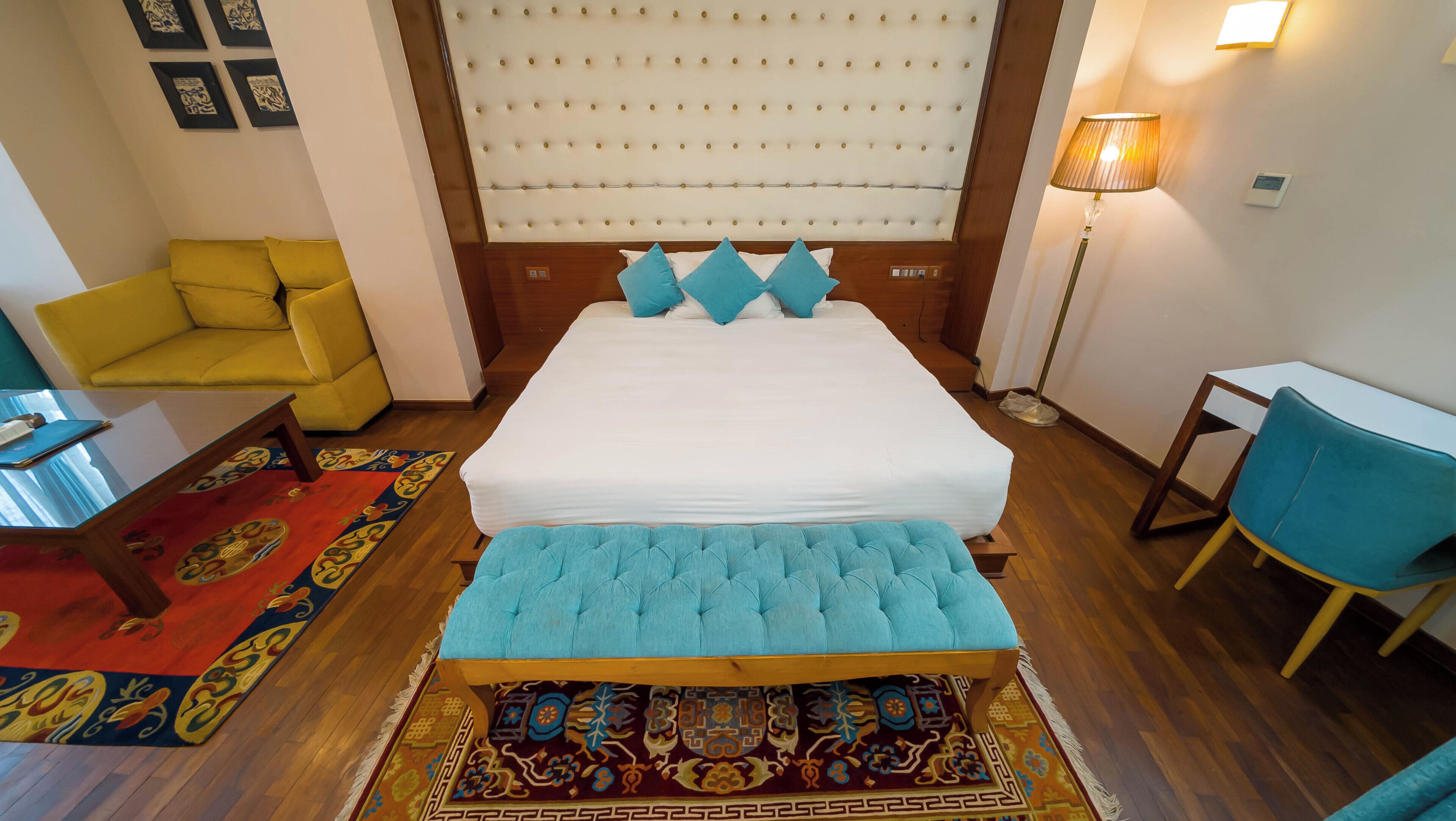 Ein Hotelzimmer mit einem großen Bett, einem gelben Sessel, einem blauen Stuhl, einem kleinen Tisch und einer Stehlampe.