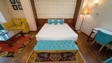 Ein Hotelzimmer mit einem großen Bett, einem gelben Sessel, einem blauen Stuhl, einem kleinen Tisch und einer Stehlampe.