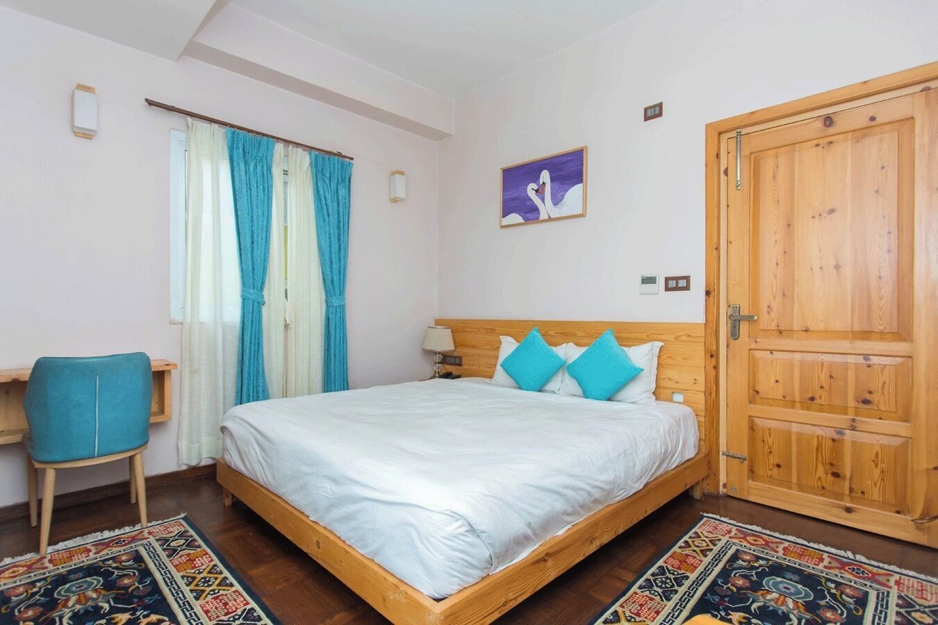 A bedroom with a wooden bed, a desk, a chair, a door, and a window with curtains.