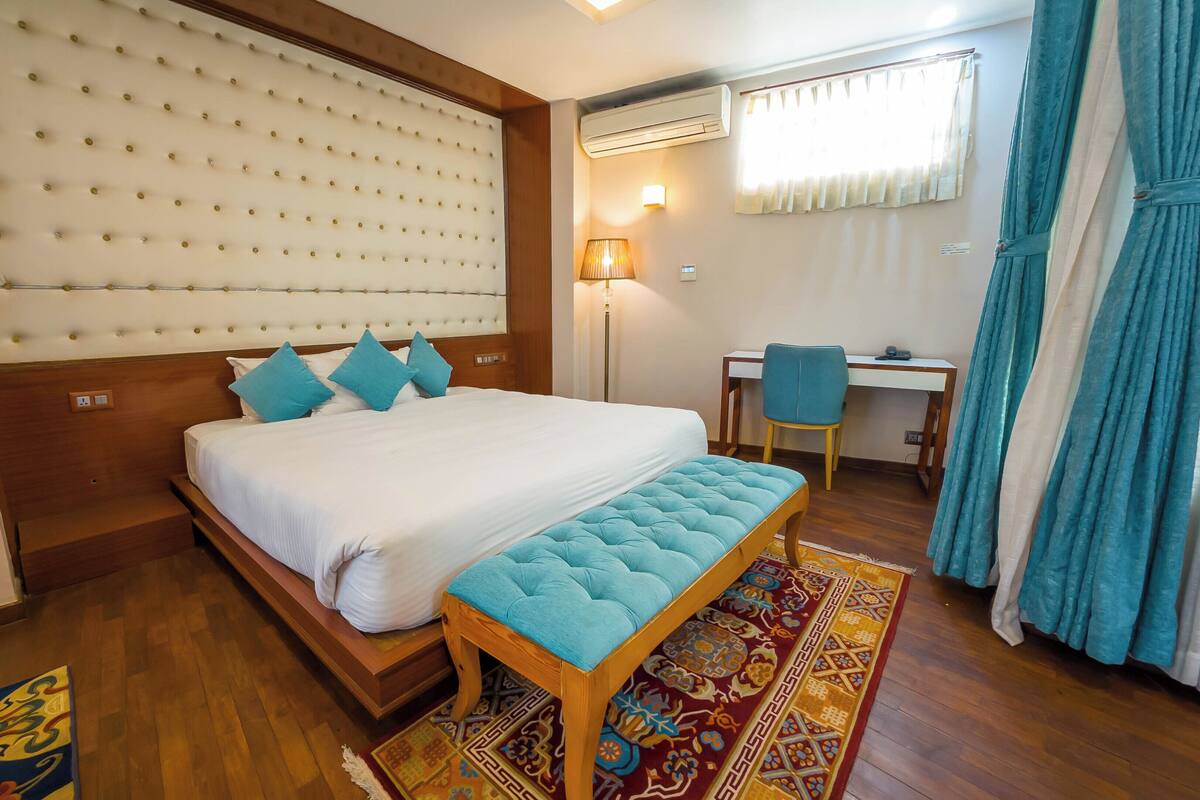 A hotel room with a large bed, a desk, a chair, and a window with curtains.