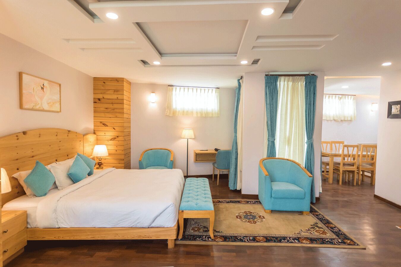 A bedroom with a wooden bed, a desk, two chairs, a bench, and a dining area with a table and chairs.