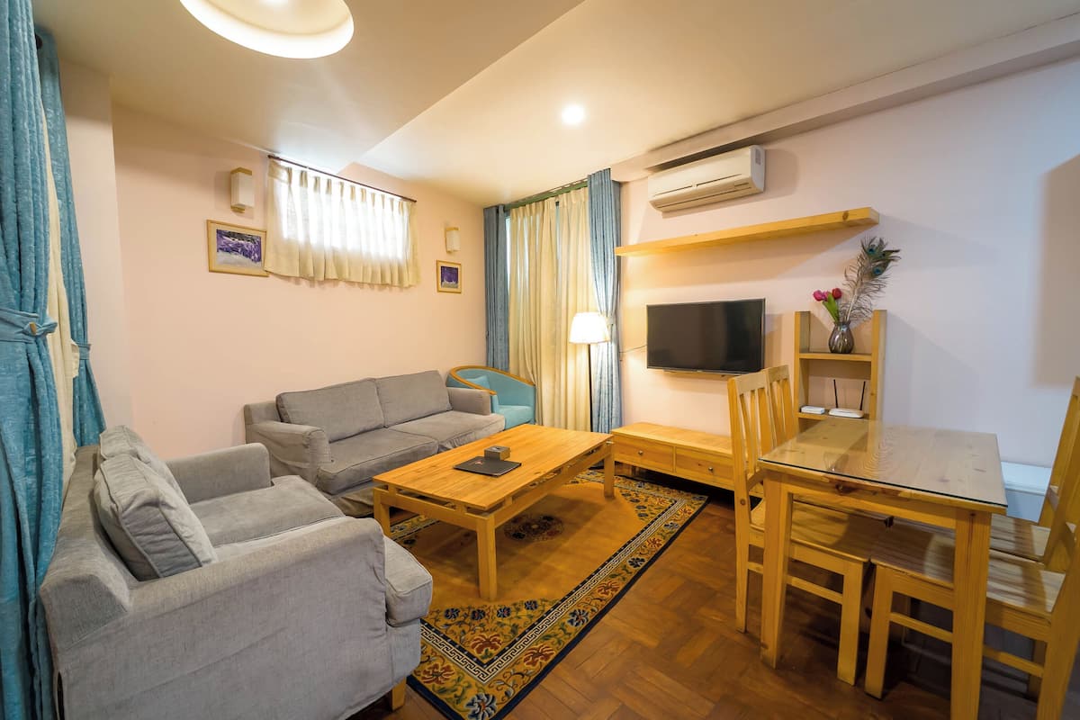 A living room with a sofa, a coffee table, a TV, and a dining area with chairs and a table.