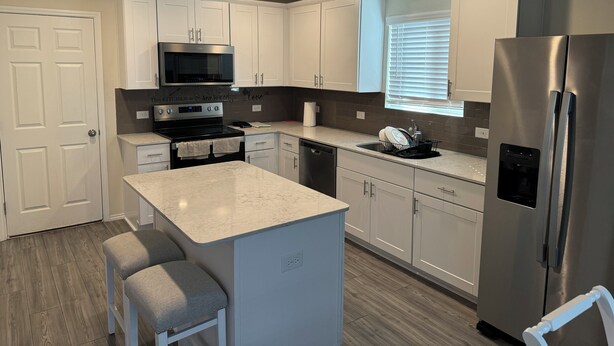 A modern kitchen with white cabinets, a stainless steel refrigerator, a built-in oven, and a microwave.
