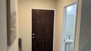 A hallway with a wooden door, a painting on the wall, and a white sink in the adjacent room.