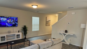 A living room with a flat-screen TV, a gray sofa, a small coffee table, and a white console table with a plant.