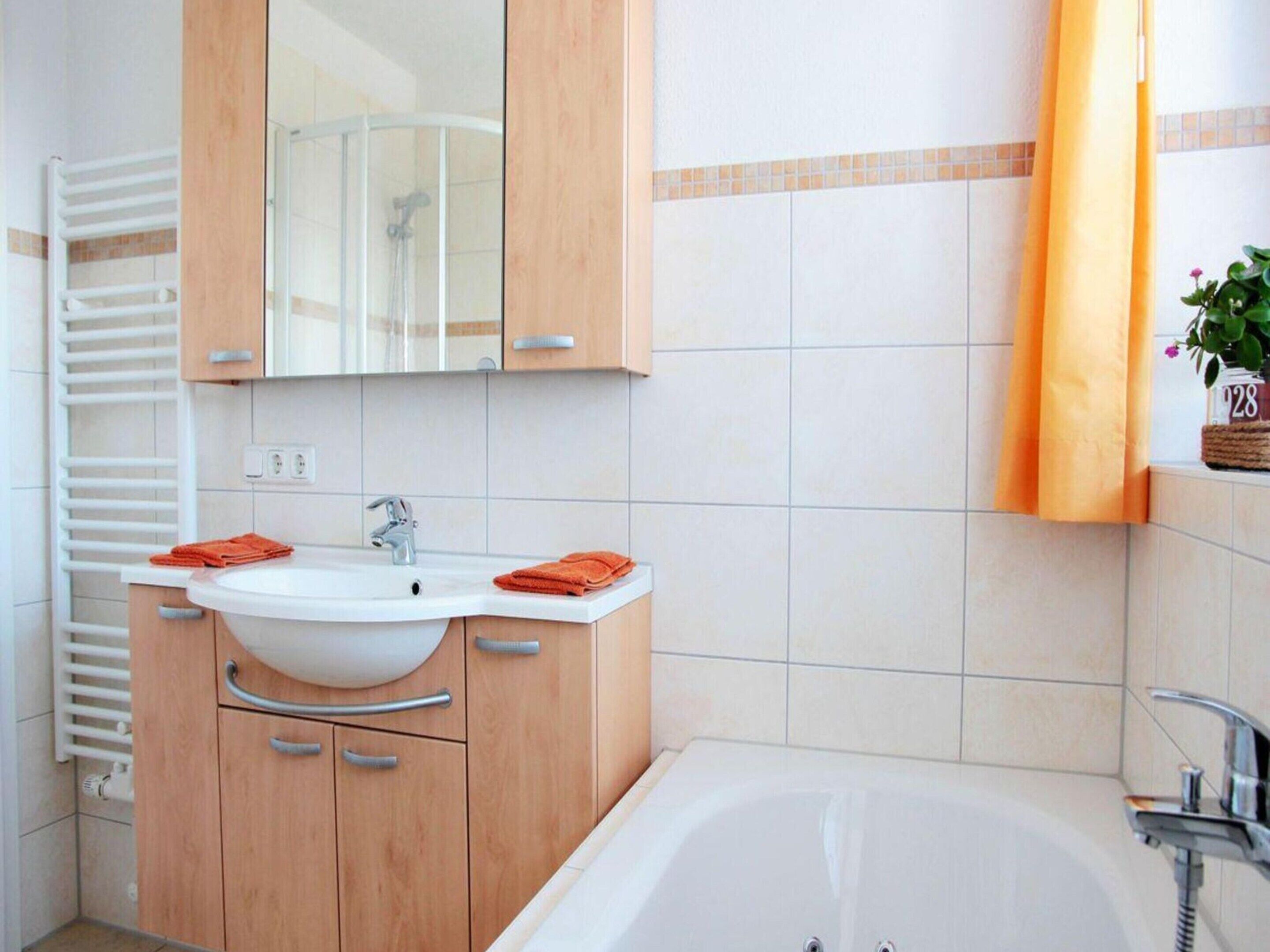 Un baño con una bañera blanca, un lavabo doble con dos espejos, armarios de madera y un perchero para toallas.