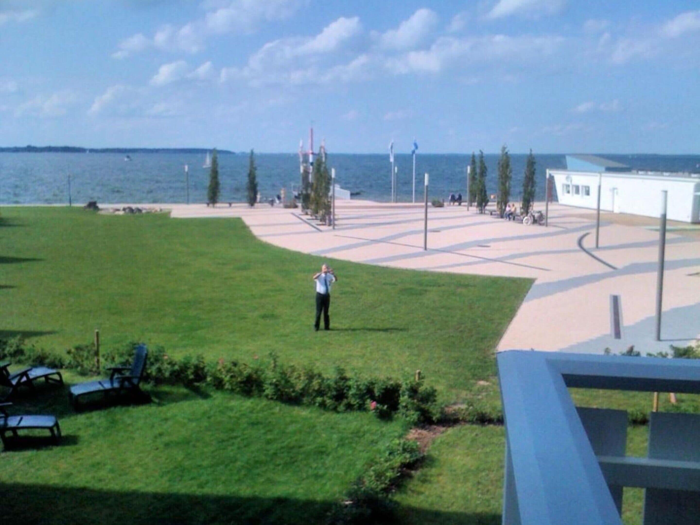 A grassy area with a pathway leading to a body of water, a white building, and a few trees.