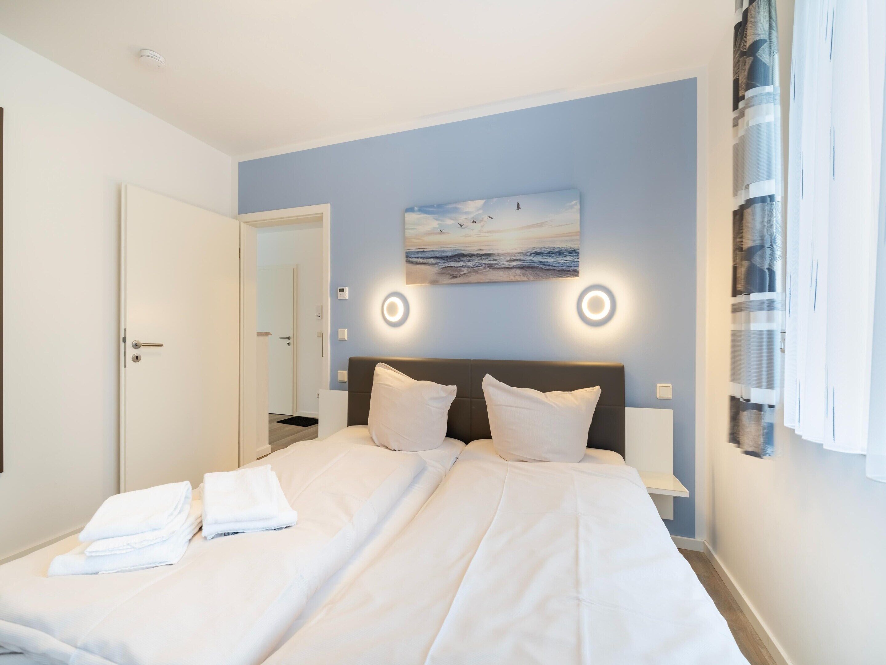 Une chambre d’hôtel avec un lit, un tableau et une fenêtre avec des rideaux.