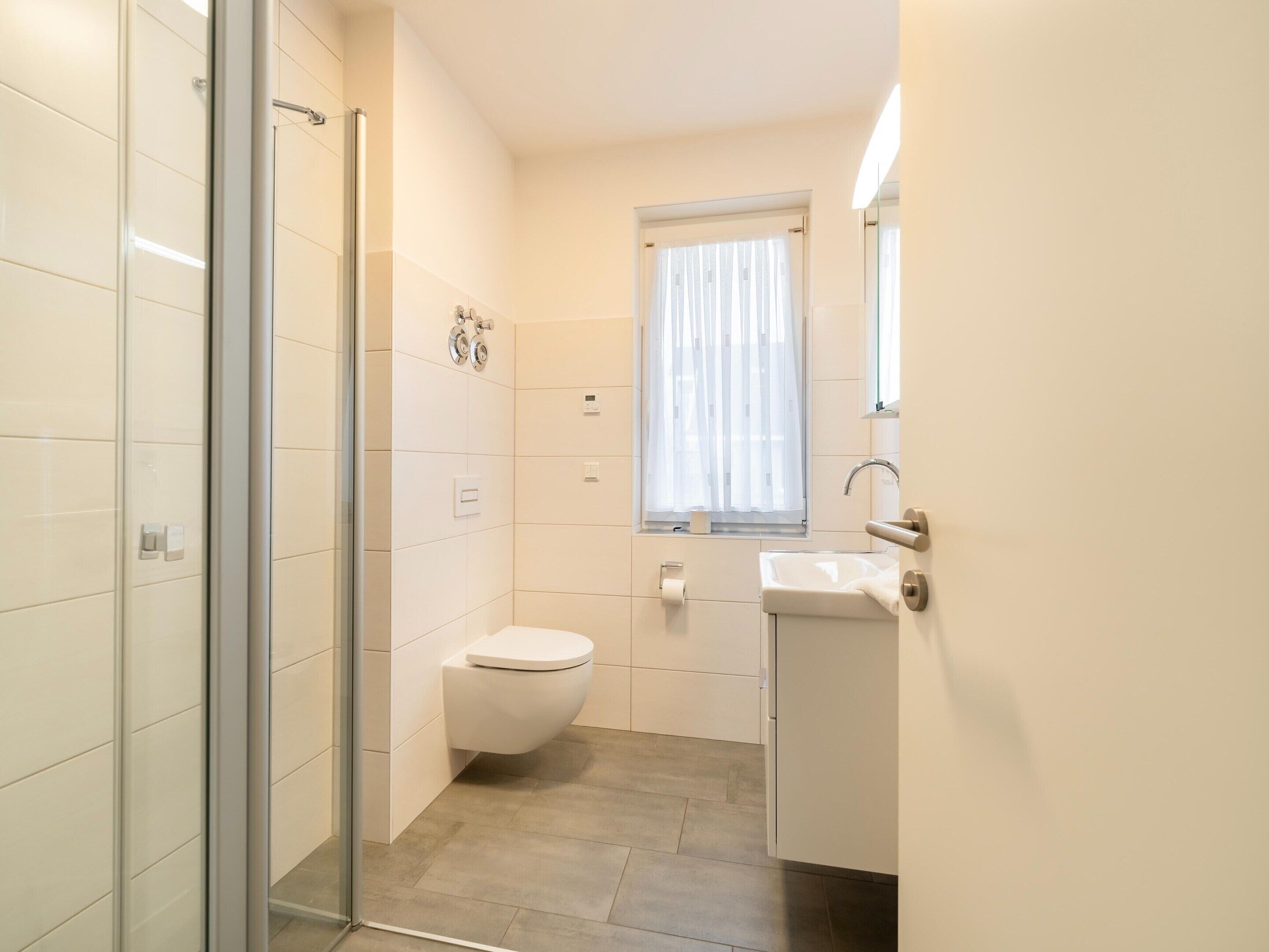 A modern bathroom with a glass shower enclosure, a toilet, and a sink with a mirror above it.