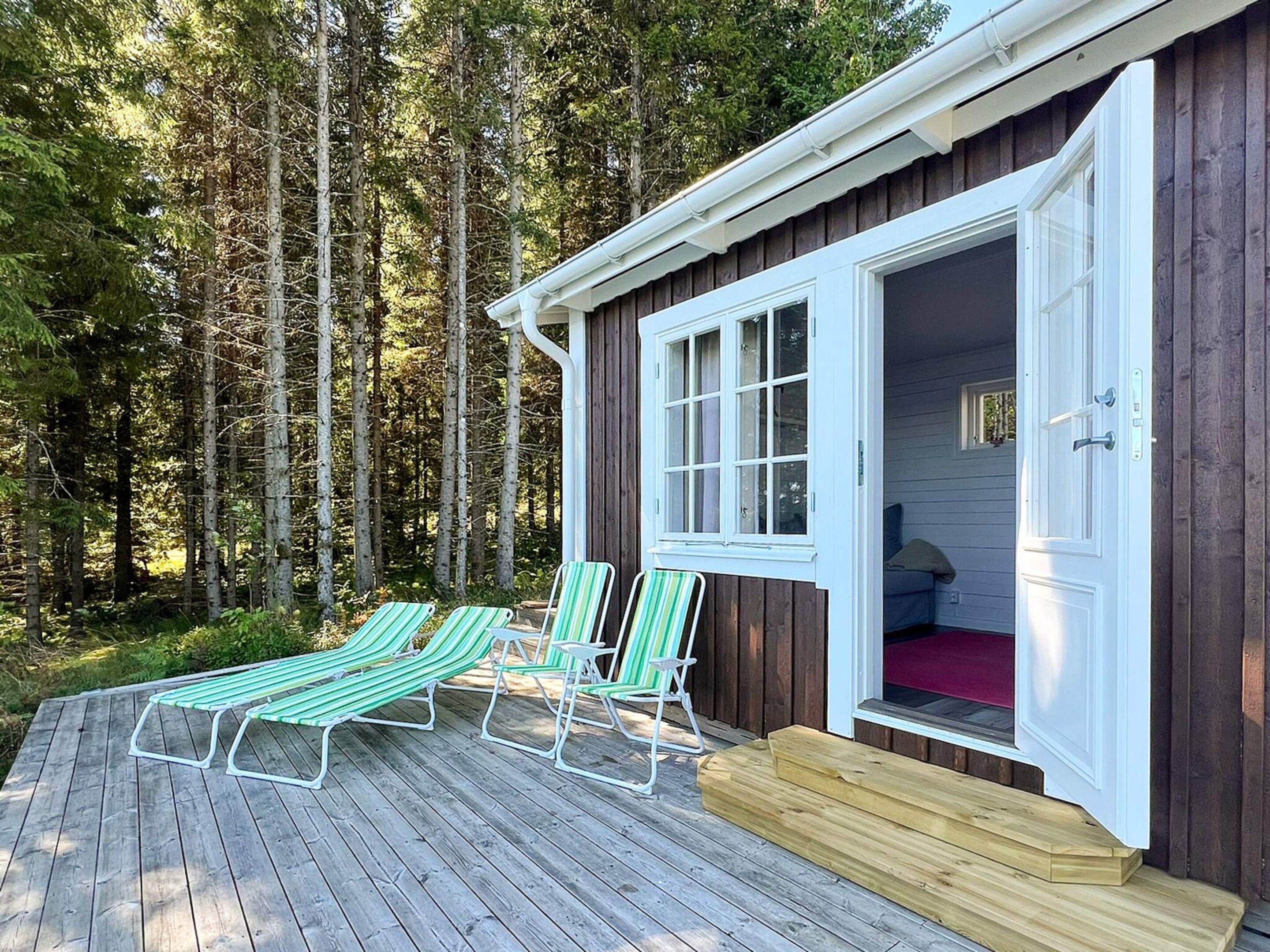A wooden cabin with a deck, two green-striped lounge chairs, and a door leading inside.