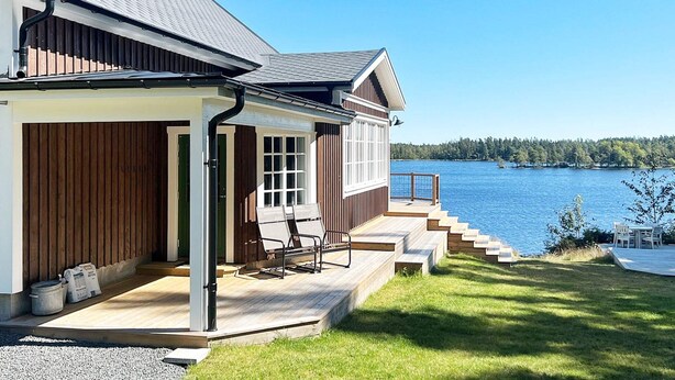 Uma casa com varanda coberta, vista para um lago e um deck com móveis de exterior.