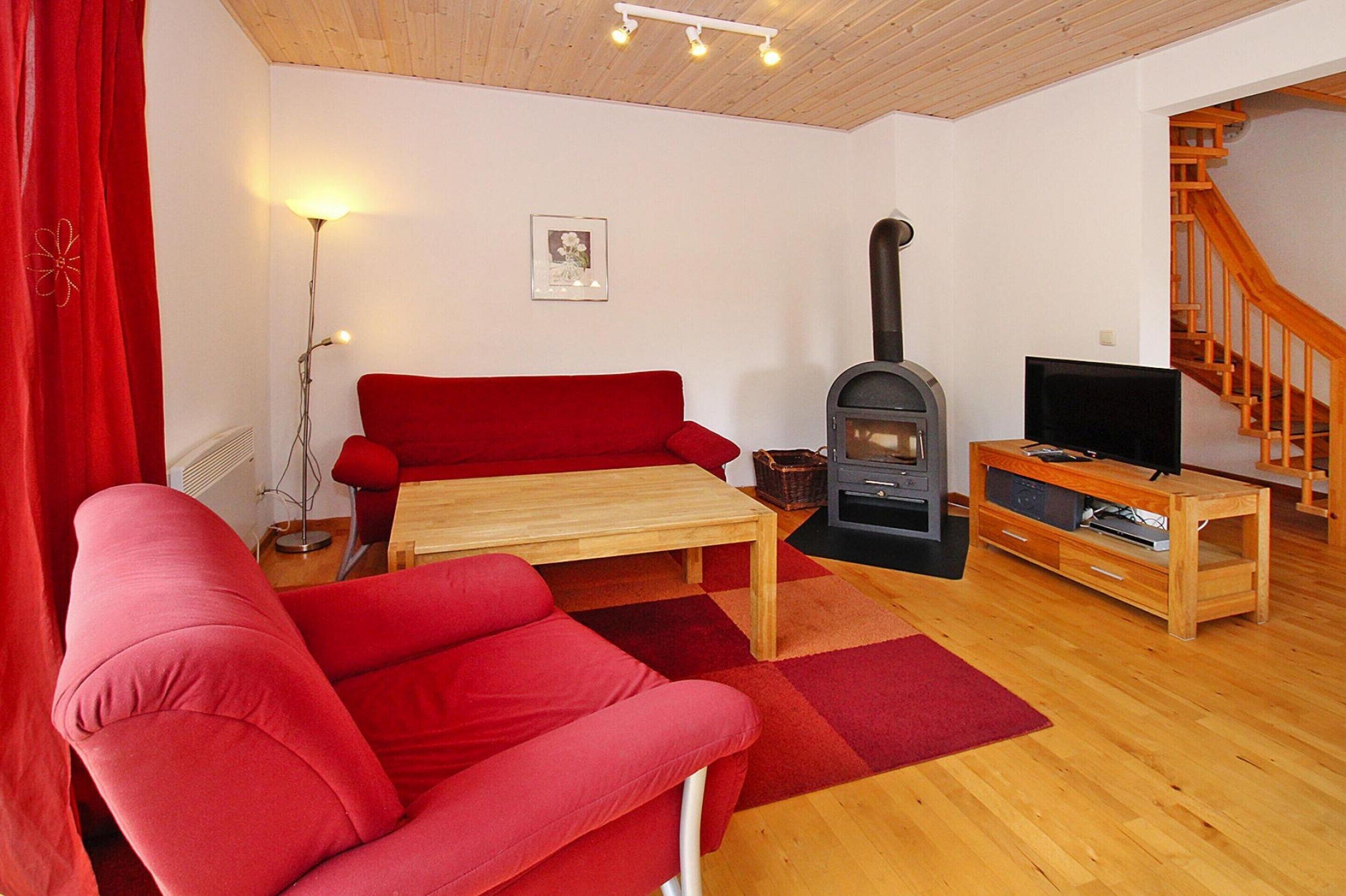 A cozy living room with a red sofa, a wooden coffee table, a fireplace, and a TV stand.