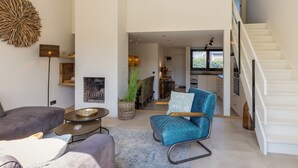 A spacious living area with a sofa, a blue armchair, and a coffee table. A staircase leads to a kitchen area. - Holiday Home Nieuwvliet Near Beach & Dunes (Nieuwvliet)