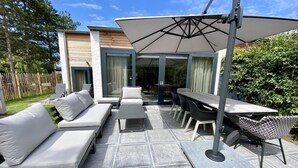 An outdoor patio with a sofa, chairs, a table, and an umbrella. - Holiday Home Nieuwvliet Near Beach & Dunes (Nieuwvliet)