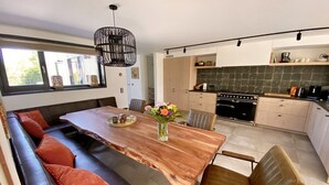 A modern kitchen with a wooden dining table, a built-in bench, and a hanging light fixture. - Holiday Home Nieuwvliet Near Beach & Dunes (Nieuwvliet)