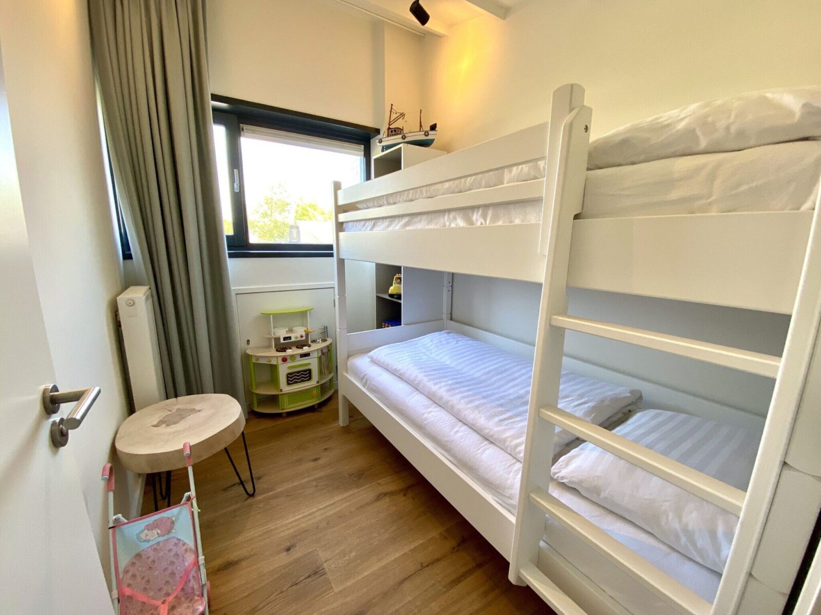 A bunk bed room with a small play kitchen set and a window with curtains.