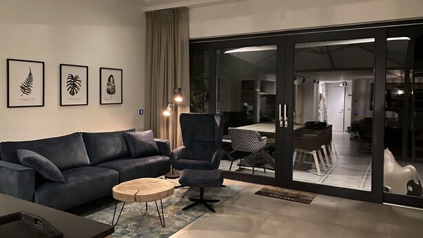 A modern living room with a dark blue sofa, a round coffee table, and a glass door leading to a dining area. - Holiday Home Nieuwvliet Near Beach & Dunes (Nieuwvliet)