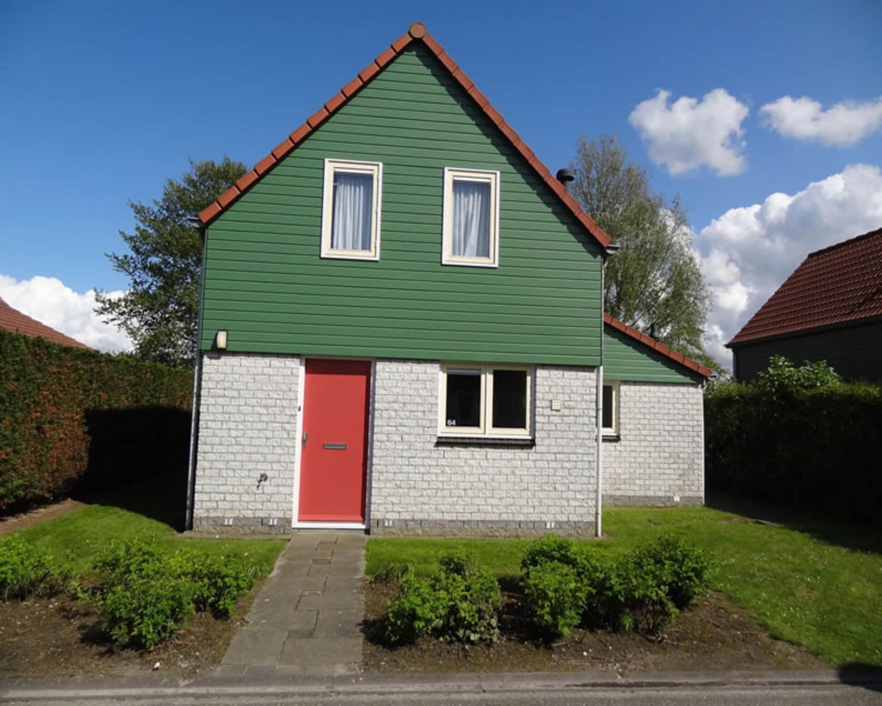 A two-story house with a red door, white-framed windows, and a green roof.