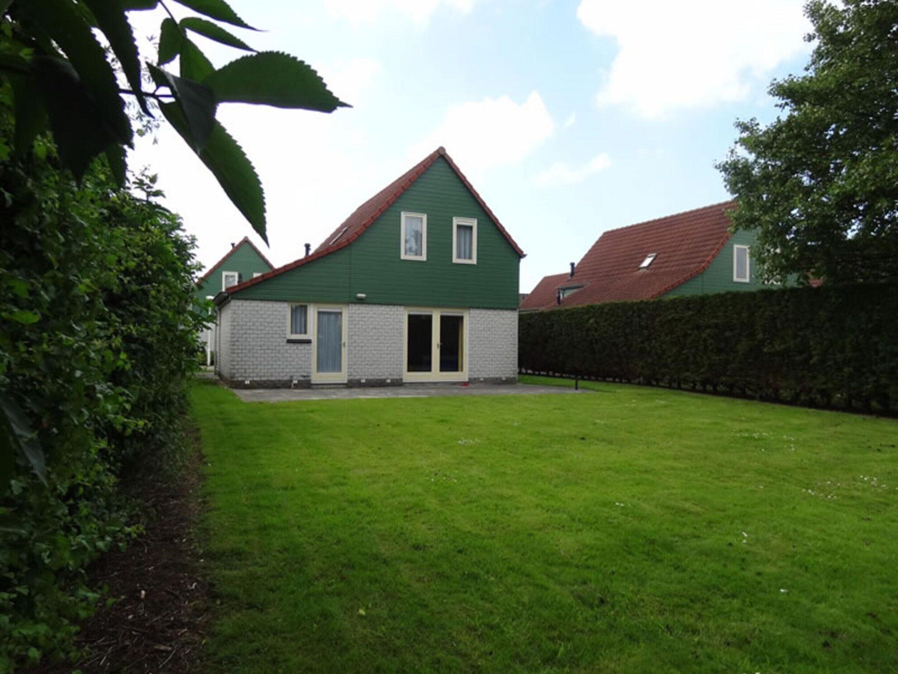 A two-story house with a green roof and white walls, a front door, and a small front yard.