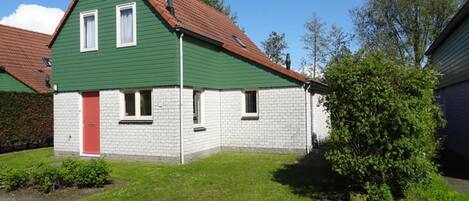 A two-story house with a green exterior and a red door, surrounded by a well-maintained lawn and a small garden.