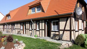 A traditional half-timbered building with a sloped red roof, a satellite dish, and outdoor seating. - Ferienwohnung auf Usedom im Lepels Hof bis zu 5 P (Luetow)