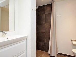 Et badeværelse med en hvid vask, et spejl, en bruser med bruseforhæng og et toilet.