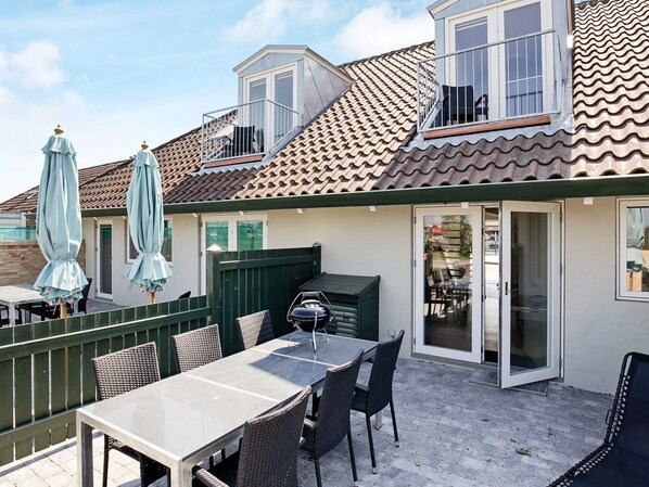 En terrasse med et bord, stole, grill og parasoller.