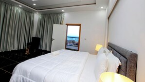 Une chambre d’hôtel avec un grand lit, un bureau, une chaise et une vue sur la mer par la fenêtre.