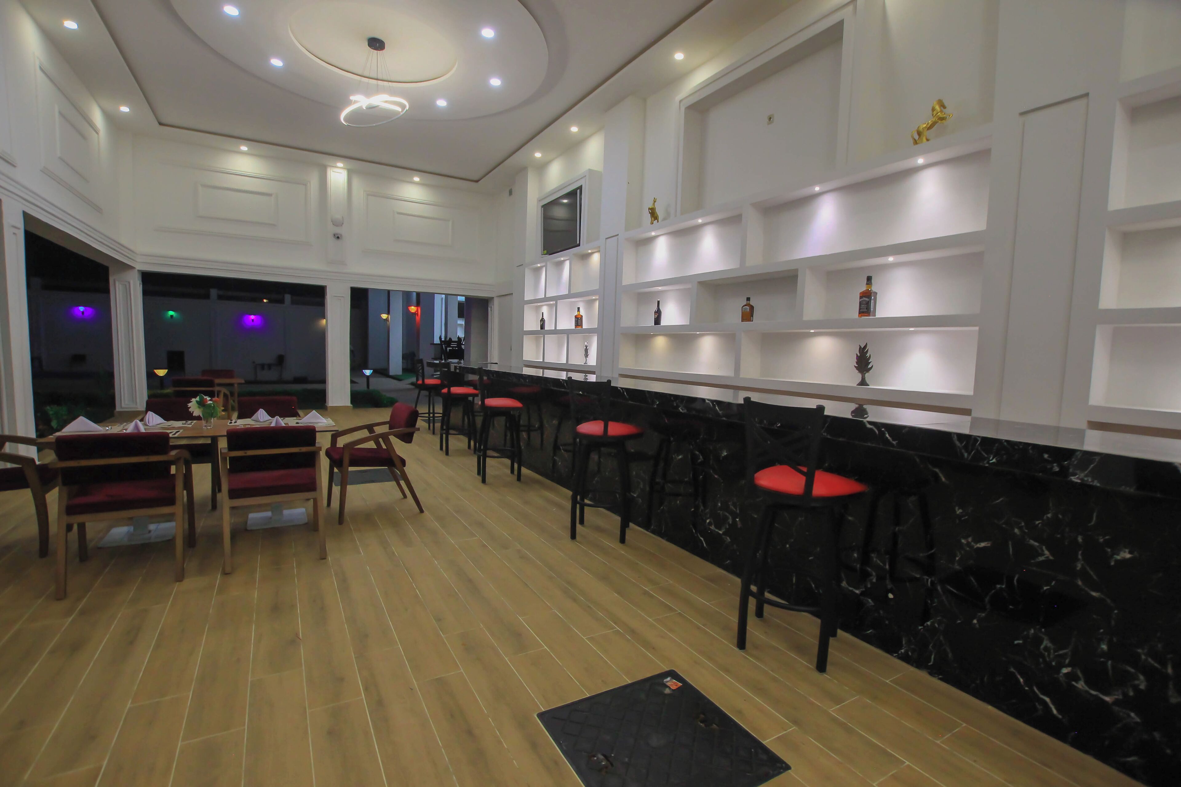 Un espace bar avec des chaises et des tables en bois, un comptoir en marbre noir et des étagères remplies de bouteilles.