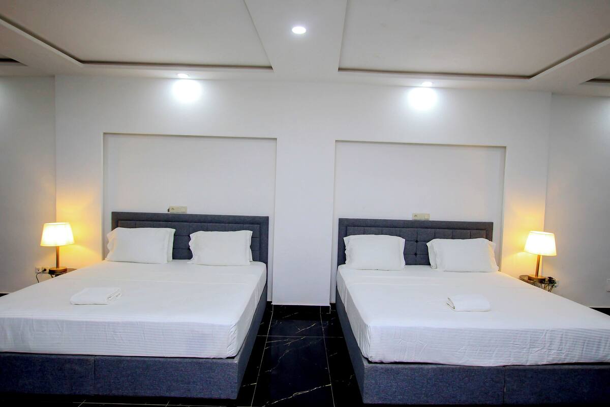 A hotel room with two beds, each with a headboard, a nightstand, and a lamp.