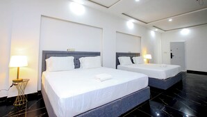 Une chambre d’hôtel avec deux lits, chacun doté d ’une tête de lit grise, de draps blancs et d’une lampe de chevet. La chambre présente un design moderne, avec un sol en marbre noir et un plafond blanc agrémenté d’un éclairage encastré.