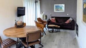 Moderni olohuone, jossa on pyöreä puinen pöytä, nahkaiset nojatuolit, tummanruskea sohva ja seinälle asennettu televisio.