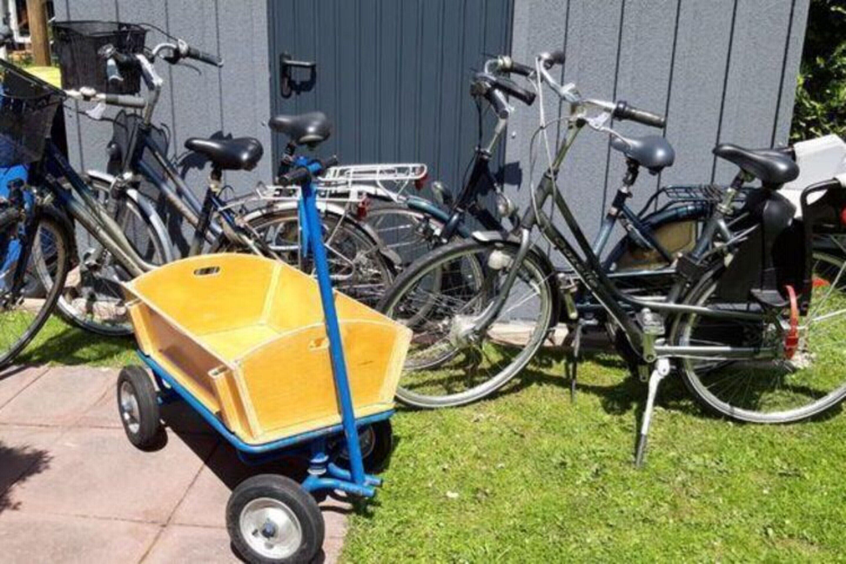 A yellow wheelbarrow with blue handles in front of bicycles parked against a building.