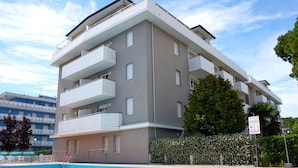 A multi-story building with balconies and a swimming pool in front.