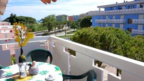 A balcony with a table set for two, a vase with flowers, and a view of a blue building and trees.