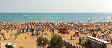 A beach with rows of sunbeds and umbrellas, a playground, and a few people walking.