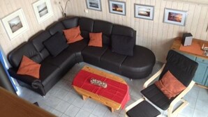 A living room with a black sectional sofa, a red ottoman, and two wooden chairs. - Skandinavisches Ferienhaus in Mirow (Mirow)