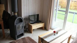 A cozy living room with a wood-burning stove, a television, and a bench. - Ferienhaus im Skandinavischen Stil (Mirow)
