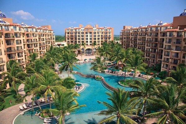 Ein Resort mit mehreren Gebäuden, einem zentralen Poolbereich, der von Palmen umgeben ist, und Blick auf den Ozean.