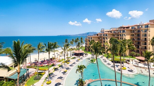 Un resort con piscina, palmeras y vista al mar.