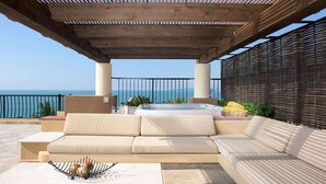 Un área de estar techada al aire libre con sofá y un jacuzzi, con vista a un cuerpo de agua.