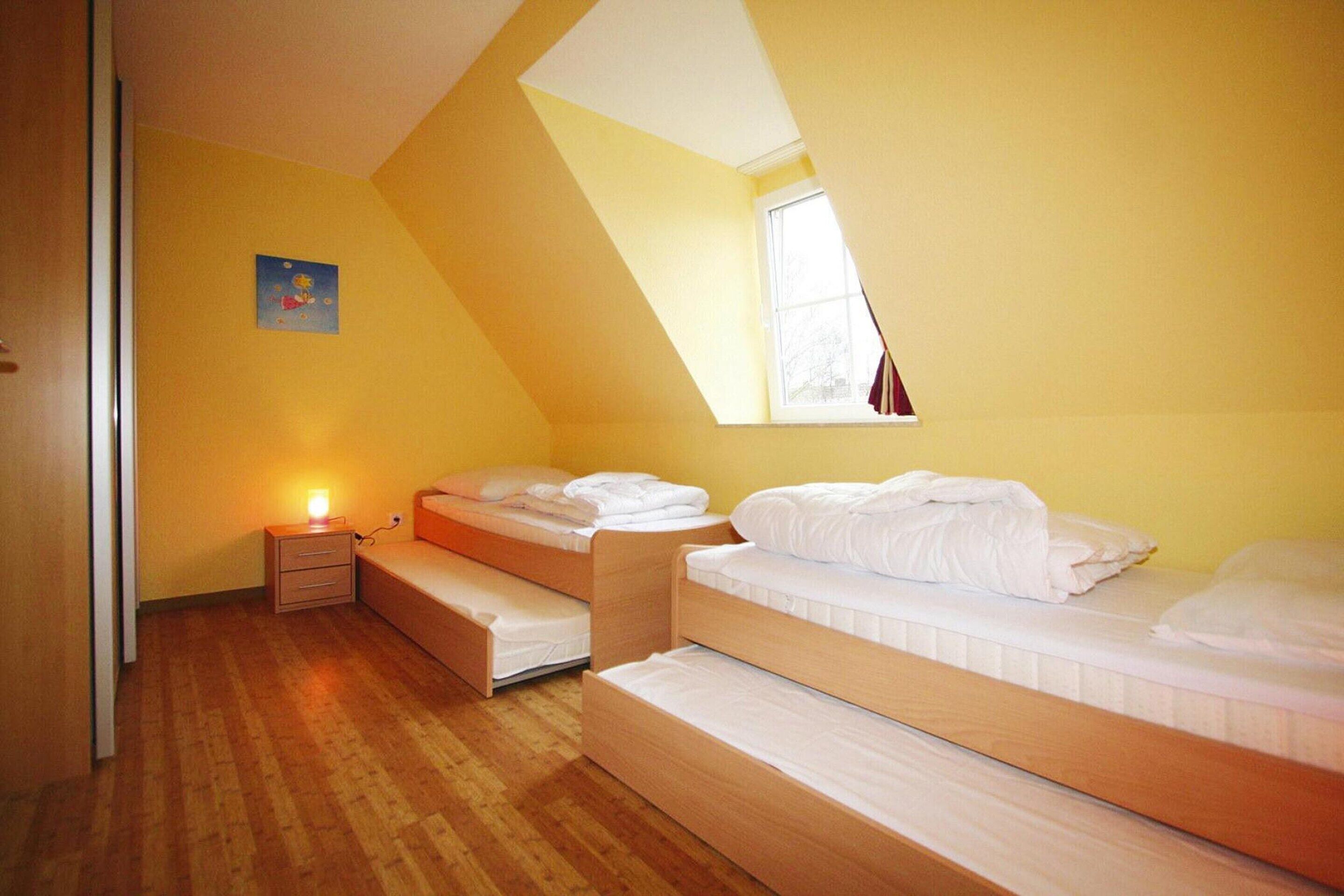 A room with three bunk beds, a small bedside table with a lamp, and a window with curtains.