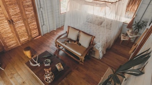 Une pièce chaleureuse avec un plancher en bois, un banc rembourré, une petite table agrémentée d’objets décoratifs et un lit à baldaquin.