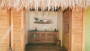 Une salle de bain rustique avec des meubles en bois, une étagère contenant des articles de toilette et un toit de chaume.