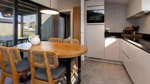 A modern kitchen with a dining area, including a wooden table and chairs, a built-in oven, and a large window. - Waterfront Stay w/ Pets (Delfstrahuizen)