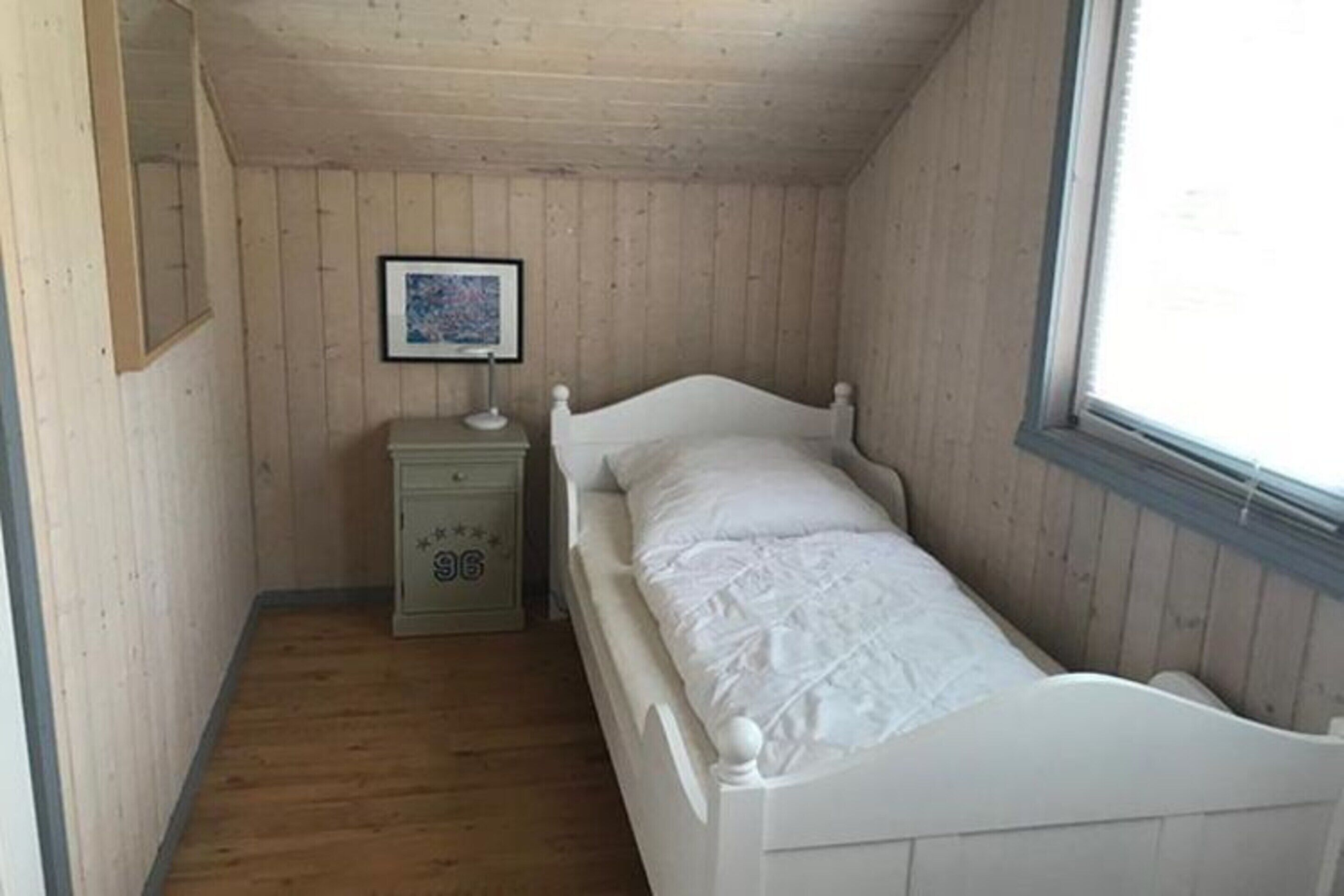 A small, single-bed room with wooden walls and a window.