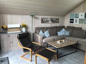 En moderne stue med sofa, to lænestole, sofabord og et tv på væggen.