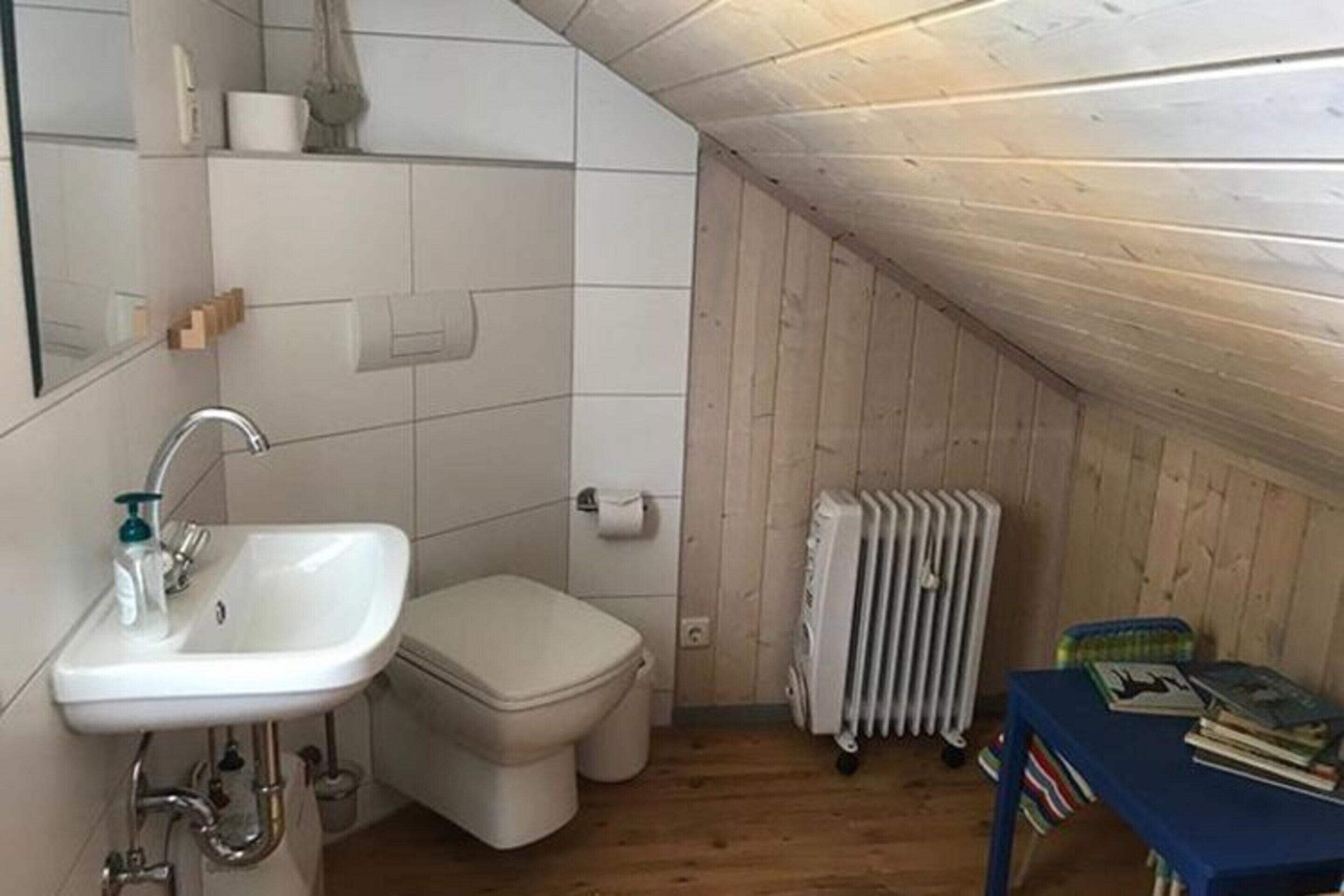 A small, compact bathroom with a white sink, toilet, and radiator.