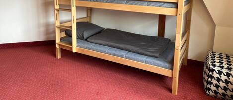 A bunk bed with grey bedding in a room with a red carpet and a houndstooth cushion.