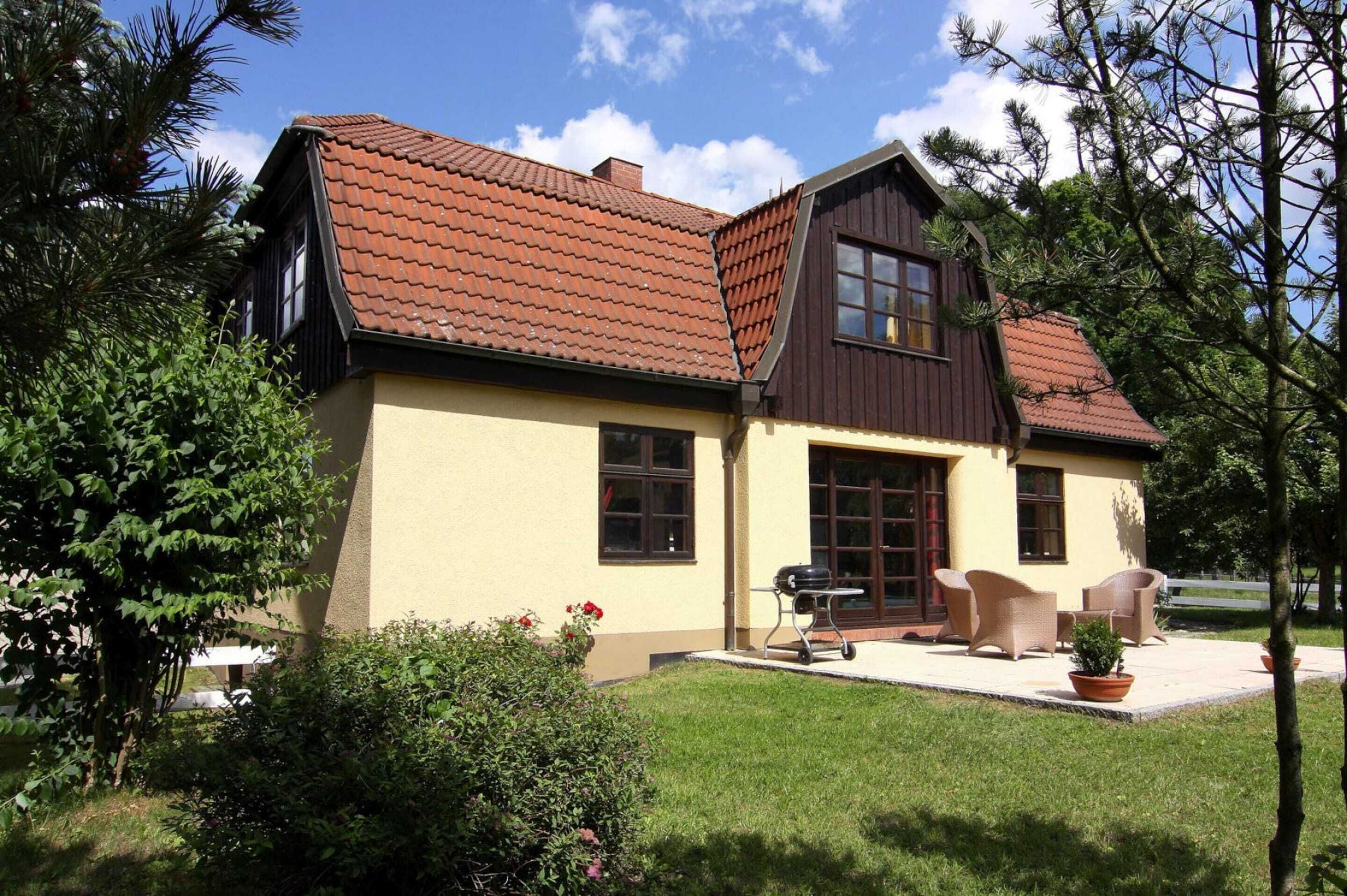 Una casa de dos pisos con techo marrón, paredes color crema y un patio con mobiliario exterior.